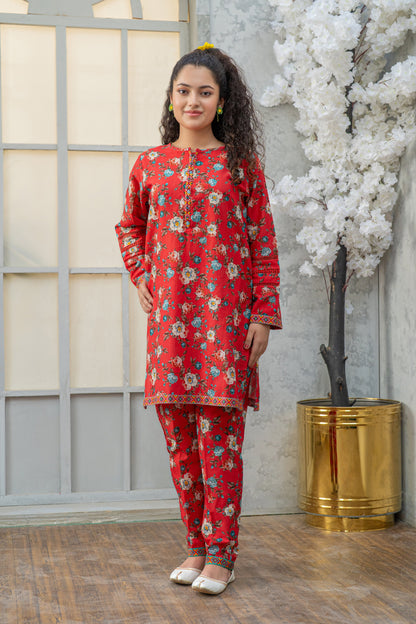 Woman wearing a red floral outfit standing in front of a decorative plant and window.
